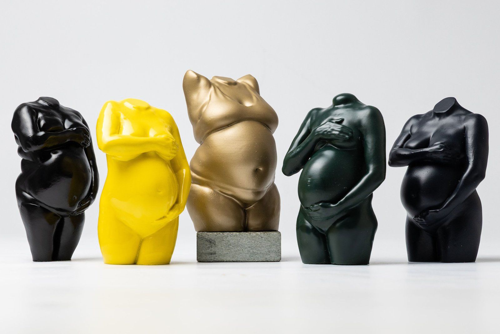 Five pregnancy sculptures in black, yellow, gold and green finishes